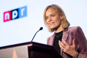 Woman in pink jacket stands at podium